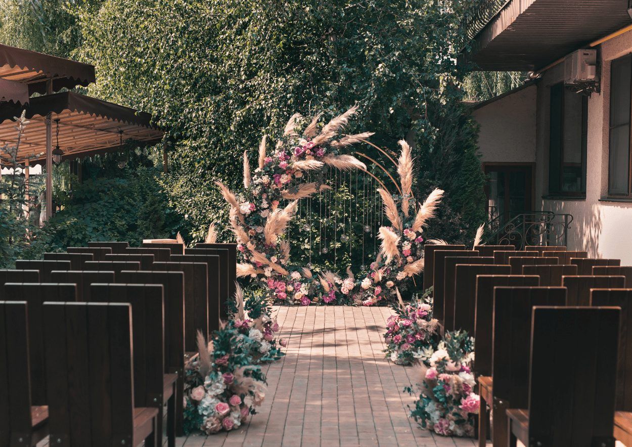 Mittelgang zwischen Holzbänken zu einem Blumenbogen mit Pampasgras